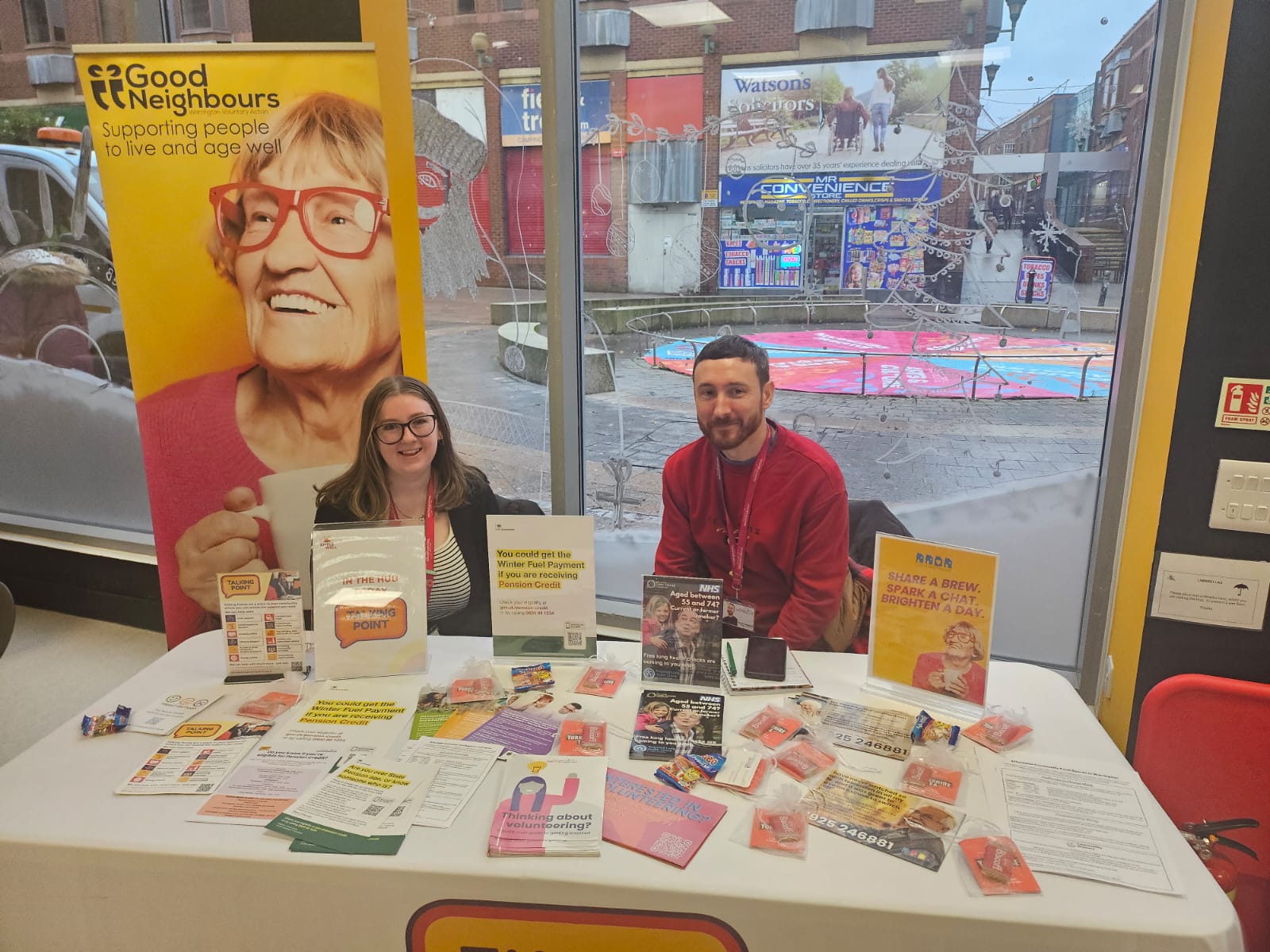 Two team members at an event with a table of leaflets