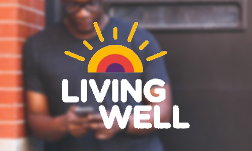 A man leaning against a wall looking at the screen of his mobile phone overlayed with the Living Well logo which is the words with a vintage styled rising sun above them